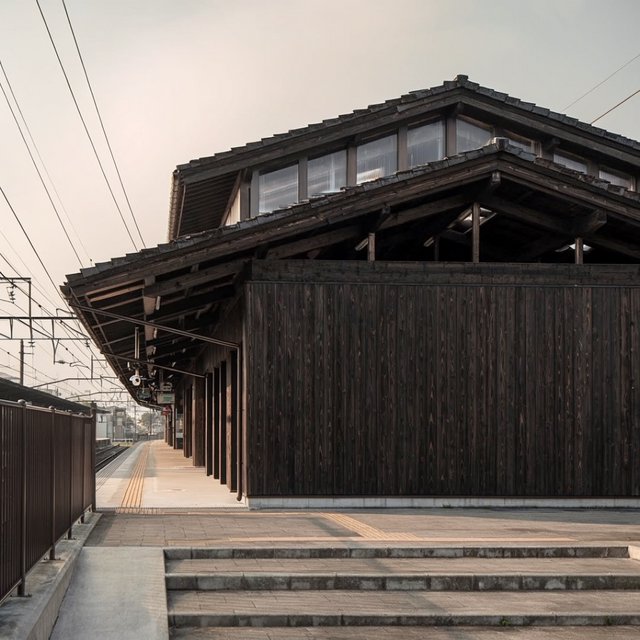 Contemporary Japanese timber train station, charred cedar cladding, pale concrete platform, broad pitched roof with exposed beams and translucent clerestories, cool morning light, viewed obliquely from the quiet approach plaza, precise straight lines and plausible structure. — Krea 2 Large