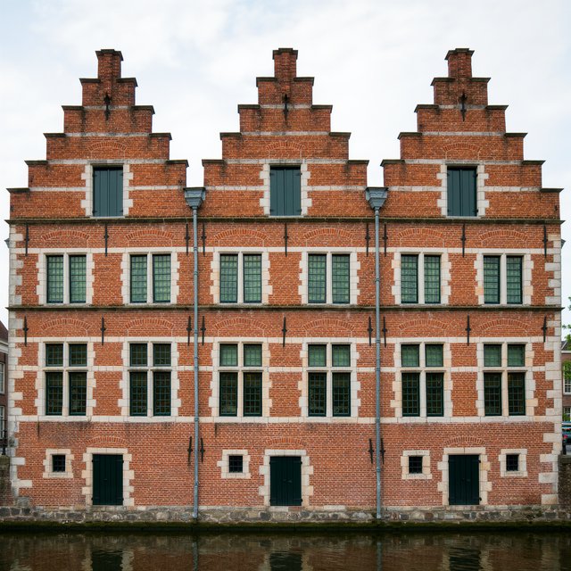 Exterior of a Dutch Renaissance canal-side archive, with warm red brick, pale stone bands, stepped gables, and tall sash windows; soft overcast light reveals the masonry, viewed from the opposite quay, with convincing structure and precise architectural lines. — Kling v3 Omni