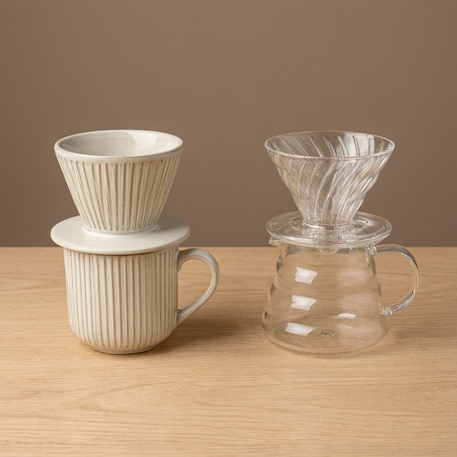 From directly overhead, an unbranded pour-over coffee set with ribbed porcelain and clear borosilicate components arranged in sequence on pale oak; warm taupe background, broad diffused softbox light and gentle side fill shape this commercial product image, no lettering. — Model 18