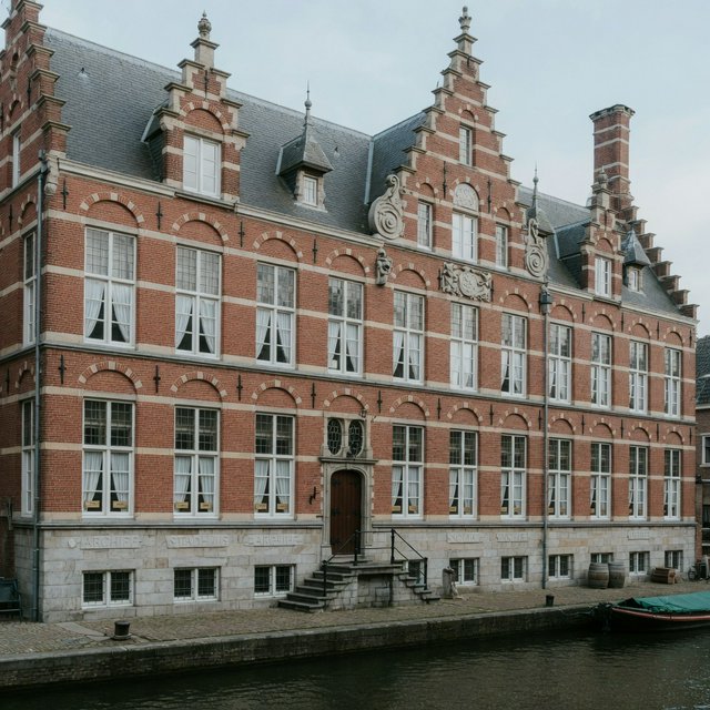 Exterior of a Dutch Renaissance canal-side archive, with warm red brick, pale stone bands, stepped gables, and tall sash windows; soft overcast light reveals the masonry, viewed from the opposite quay, with convincing structure and precise architectural lines. — Grok Imagine Image Quality