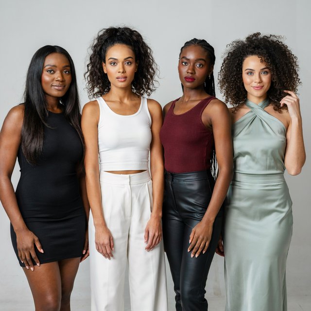 Realistic image of four women standing near each other. All are wearing fitted outfits. All are slim but still curvy Black women. Each woman has a unique, pretty face, and they all look different from one another. Full-body image. Plain background. — Model 6
