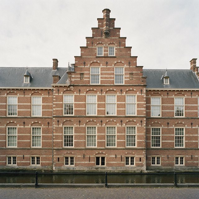 Exterior of a Dutch Renaissance canal-side archive, with warm red brick, pale stone bands, stepped gables, and tall sash windows; soft overcast light reveals the masonry, viewed from the opposite quay, with convincing structure and precise architectural lines. — Seedream 5.0 Pro