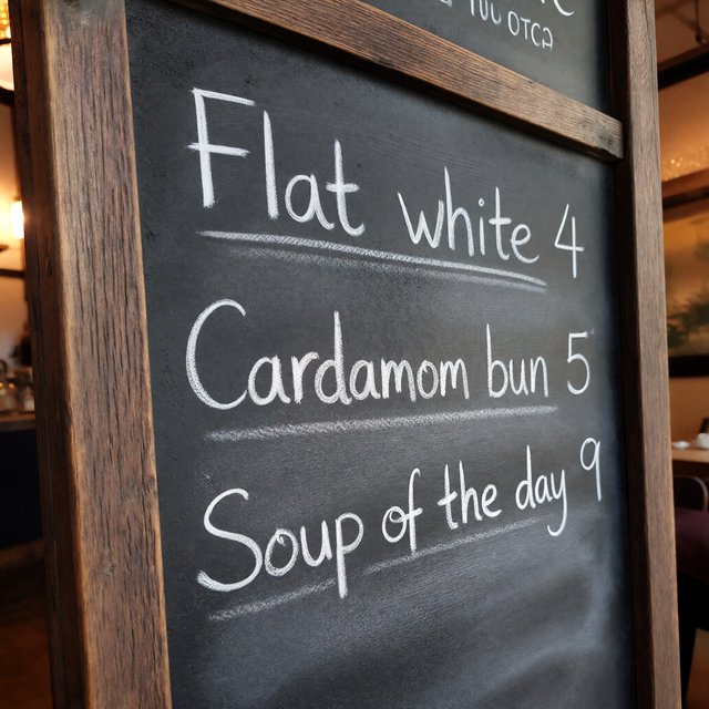 A café chalkboard listing exactly three items: "Flat white 4", "Cardamom bun 5", "Soup of the day 9", in neat chalk handwriting. — ImagineArt 1.5 Pro