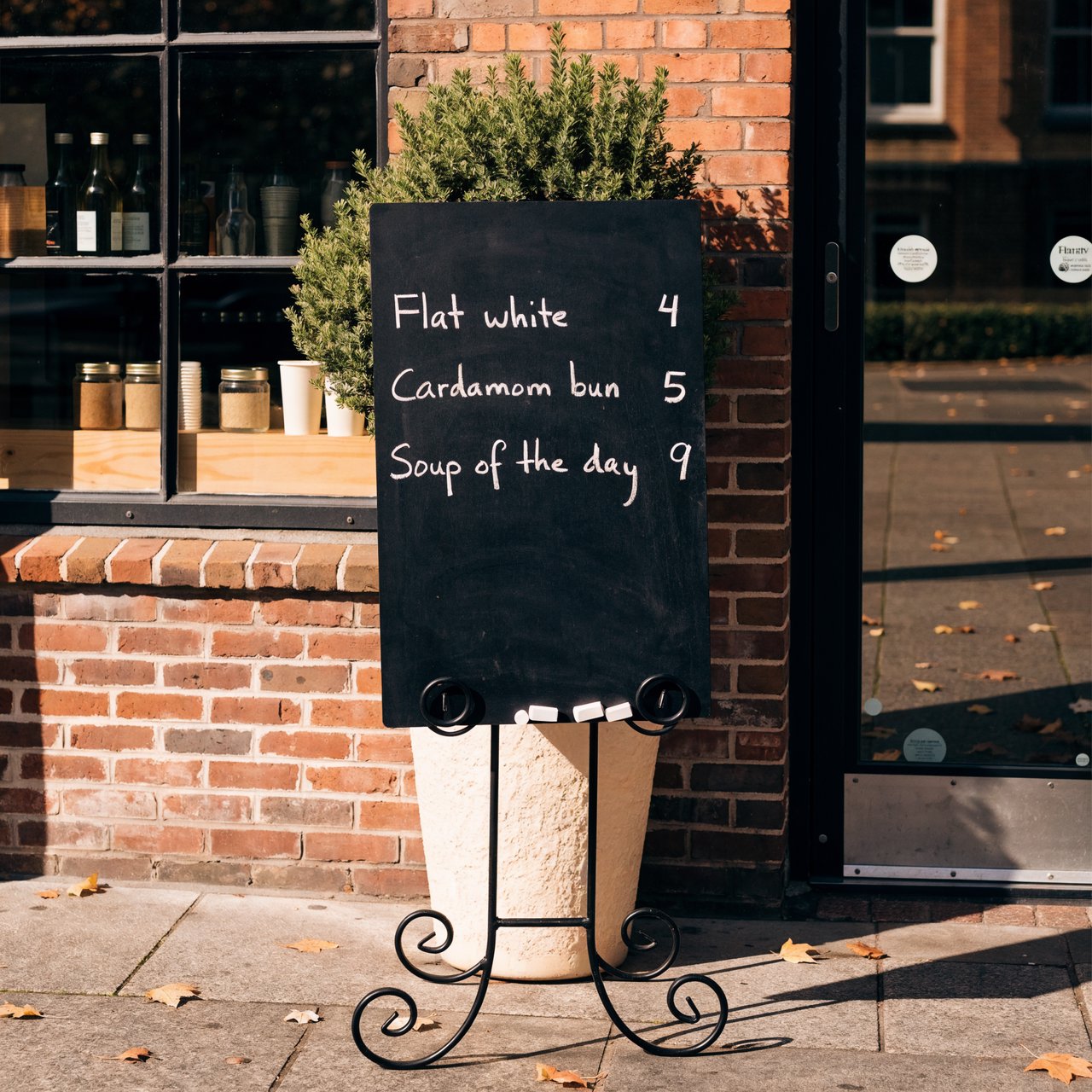 A café chalkboard listing exactly three items: "Flat white 4", "Cardamom bun 5", "Soup of the day 9", in neat chalk handwriting. — Recraft v4 Pro