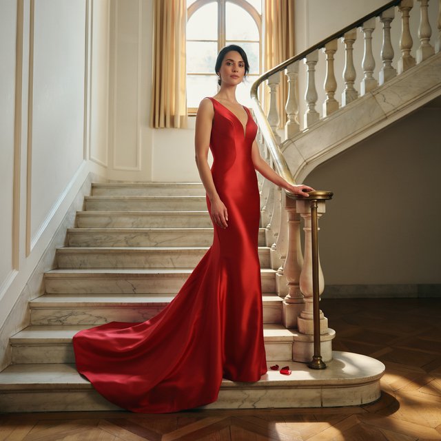 An adult woman in a floor-length red satin evening gown on a marble staircase, soft key light, confident pose, magazine cover style. — Ideogram v4