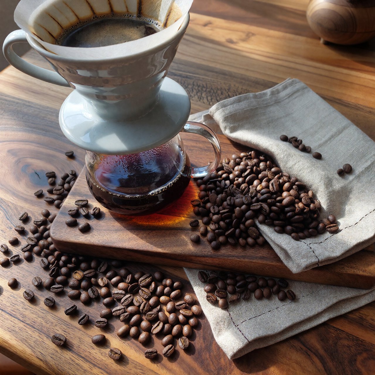 Overhead flat lay of a ceramic pour-over coffee set on oak, roasted beans scattered, a folded linen napkin, warm natural light. — ImagineArt 1.5 Pro