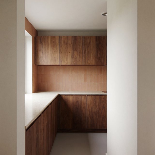Along a galley kitchen, flat-front walnut cabinets meet pale limestone counters and a matte terracotta backsplash in restrained Scandinavian modern style; soft north-window daylight reveals the worktop from the doorway, with clean aligned lines and believable supports. — Model 12