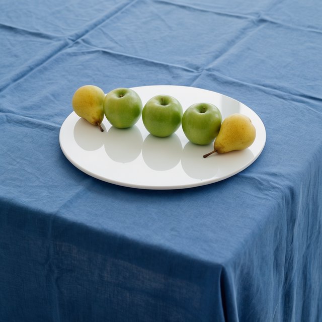 Exactly three green apples and two yellow pears on a white plate, the plate on a blue tablecloth, nothing else on the table. — Krea 2 Large