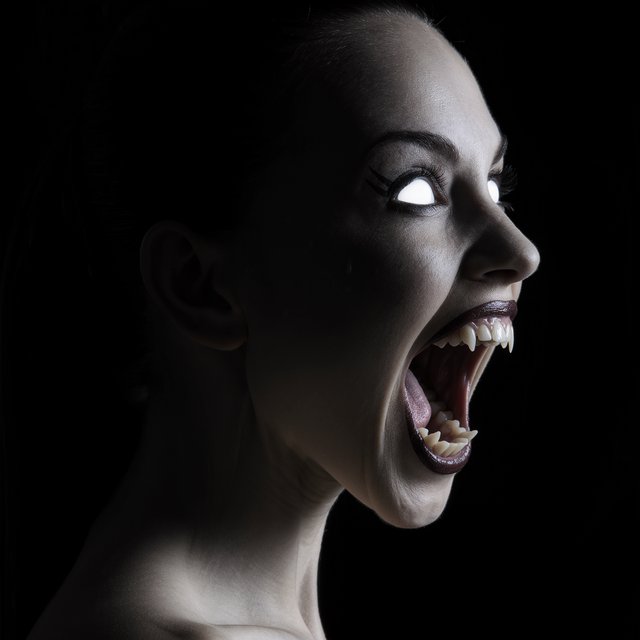 A creepy woman in side profile. Focus on the head with a slightly alien figure. Pale skin. No irises in the eyes. Mouth is open wide with very sharp, long razor teeth. Black background. Chiaroscuro effect. — Kling v3 Omni