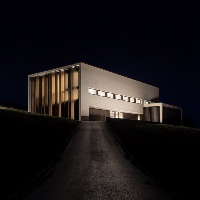 A hilltop observatory in spare contemporary architecture glows against the midnight sky, its pale concrete walls, bronze panels, and narrow windows lit from within; viewed from the access road, crisp edges and credible structural supports. — Krea 2 Large