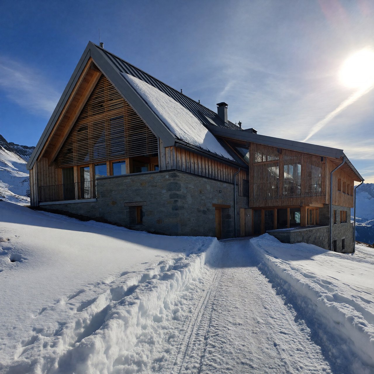 Exterior of a contemporary alpine research lodge in restrained regional modernism, rough granite walls, larch screens, steep standing-seam roof, crisp snow-bright morning light, viewed from below across a mountain footpath, sound structural geometry. — ImagineArt 1.5 Pro