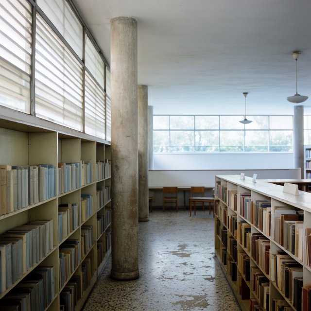 Interior of a mid-century modernist public library, with pale oak shelving, exposed concrete columns, terrazzo flooring, and a broad clerestory. Diffuse morning light crosses the reading hall, viewed from the entrance down its central aisle, with precise lines and plausible structure. — Krea 2 Large