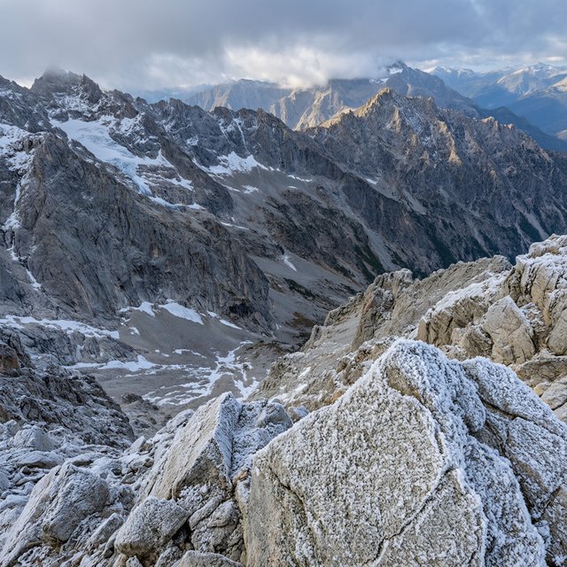 Wind combs a high granite ridge above a glacial cirque at sunrise, beneath clearing snow squalls; granular rime crusts foreground boulders while successive peaks dissolve into blue cloud shadow. — Qwen Image 3.0 Pro