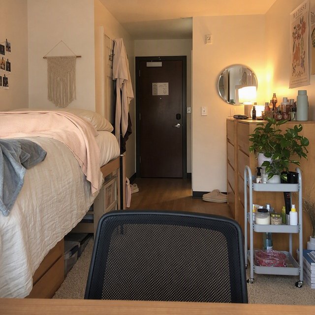 A dorm room belonging to an adult woman, photographed with a cell phone. The camera is sitting on a desk facing the empty chair and the rest of the room. — GPT Image 2