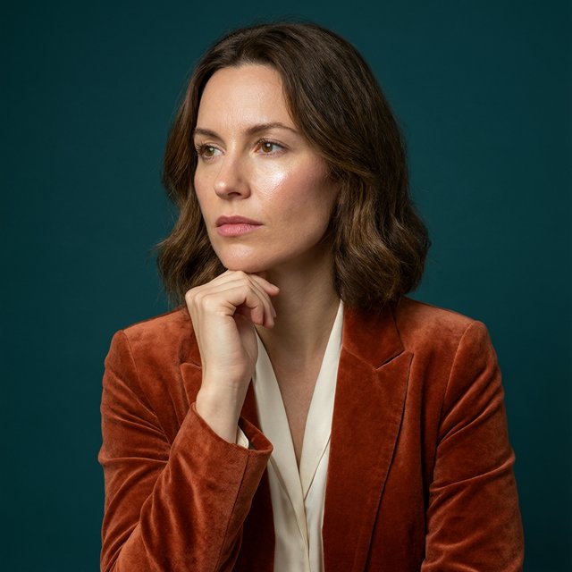 Portrait of an adult woman in her 30s wearing a rust-colored velvet jacket over an ivory blouse, one hand resting beneath her chin, thoughtful expression, deep teal studio backdrop, soft side lighting and gentle cheek highlights. — Qwen Image 3.0 Pro