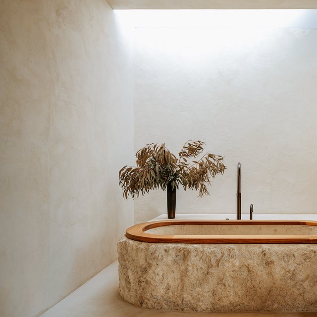 A spa bathroom with a stone tub, a skylight, plaster walls in warm white, eucalyptus in a vase, soft shadows. — Krea 2 Large