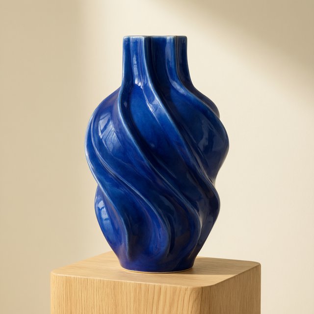 Commercial product photograph of an unbranded sculptural ceramic vase, formed from glossy cobalt porcelain, standing on a pale oak pedestal against a warm ivory background, illuminated by soft directional daylight and subtle fill. — Qwen Image 3.0