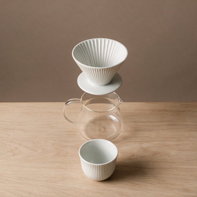From directly overhead, an unbranded pour-over coffee set with ribbed porcelain and clear borosilicate components arranged in sequence on pale oak; warm taupe background, broad diffused softbox light and gentle side fill shape this commercial product image, no lettering. — Model 20