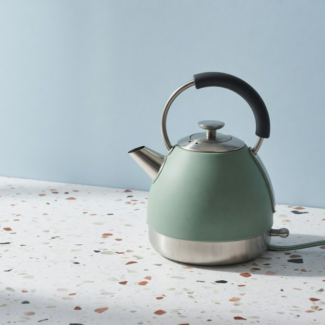 Commercial product photograph of an unbranded electric kettle made from matte sage ceramic and brushed stainless steel, resting on a white terrazzo surface against a pale blue background, with soft window light from the left and a delicate grounding shadow. — Grok Imagine Image Quality