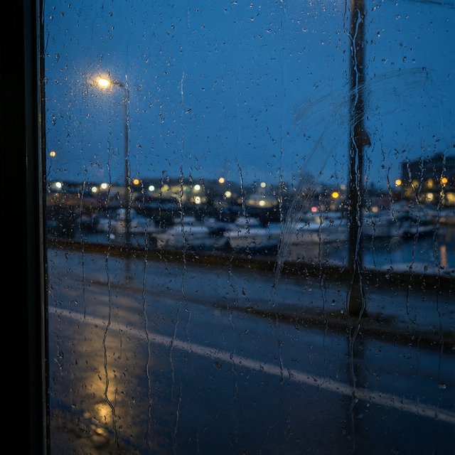Raindrops crawl down a bus shelter pane, warping blurred harbor lights beyond. A handheld evening street snapshot in cool sodium glow, shot at 50mm with shallow depth of field, catches tiny water trails and a faint wipe mark. — Qwen Image 3.0 Pro
