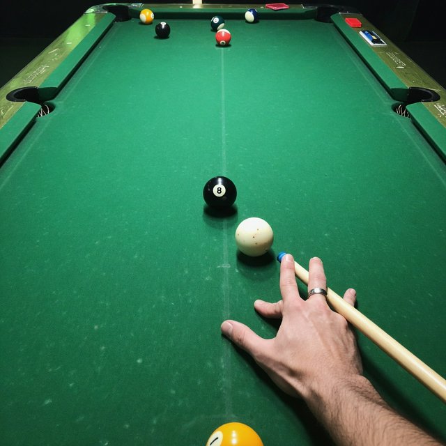 First-person perspective of an adult pool player’s left hand holding the cue, aiming the white cue ball at the black 8-ball and intending to pocket it in the center pocket. — Grok Imagine Image Quality