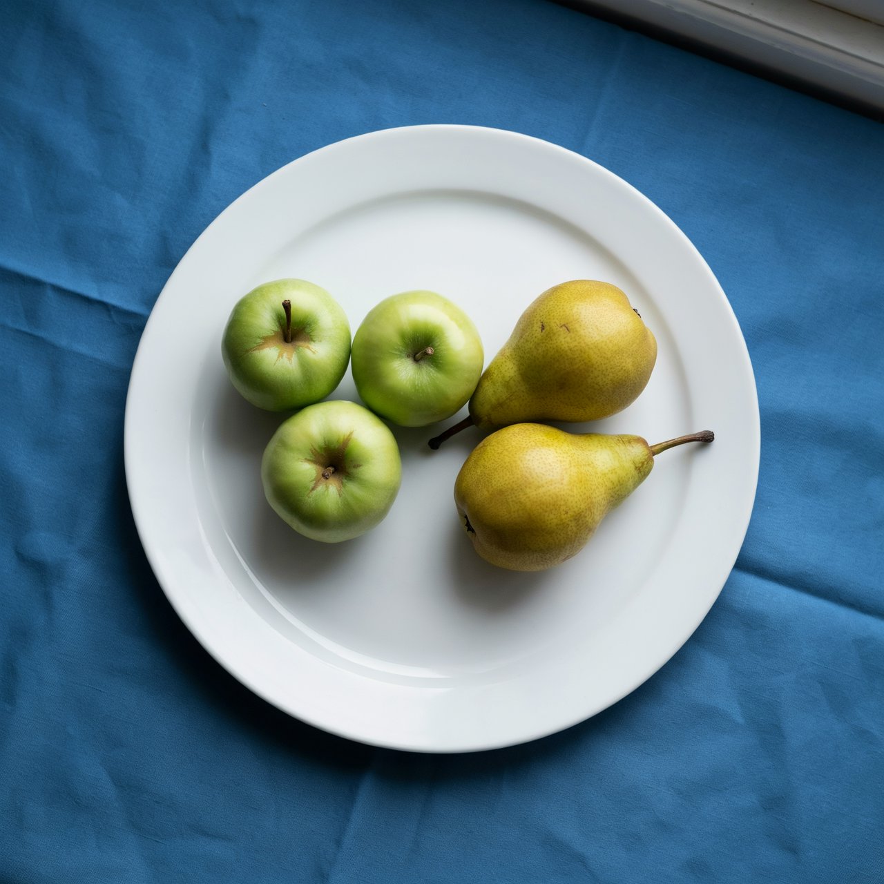 Exactly three green apples and two yellow pears on a white plate, the plate on a blue tablecloth, nothing else on the table. — Ideogram v4