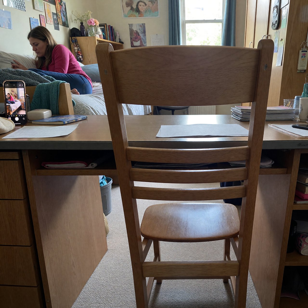 A dorm room belonging to an adult woman, photographed with a cell phone. The camera is sitting on a desk facing the empty chair and the rest of the room. — ImagineArt 1.5 Pro