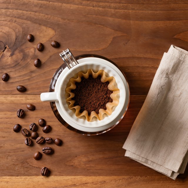 Overhead flat lay of a ceramic pour-over coffee set on oak, roasted beans scattered, a folded linen napkin, warm natural light. — Kling v3