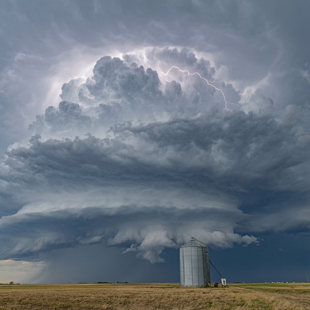 A supercell thunderstorm over flat farmland, lightning inside the cloud, a lone grain silo, dramatic but realistic. — Qwen Image 3.0 Pro