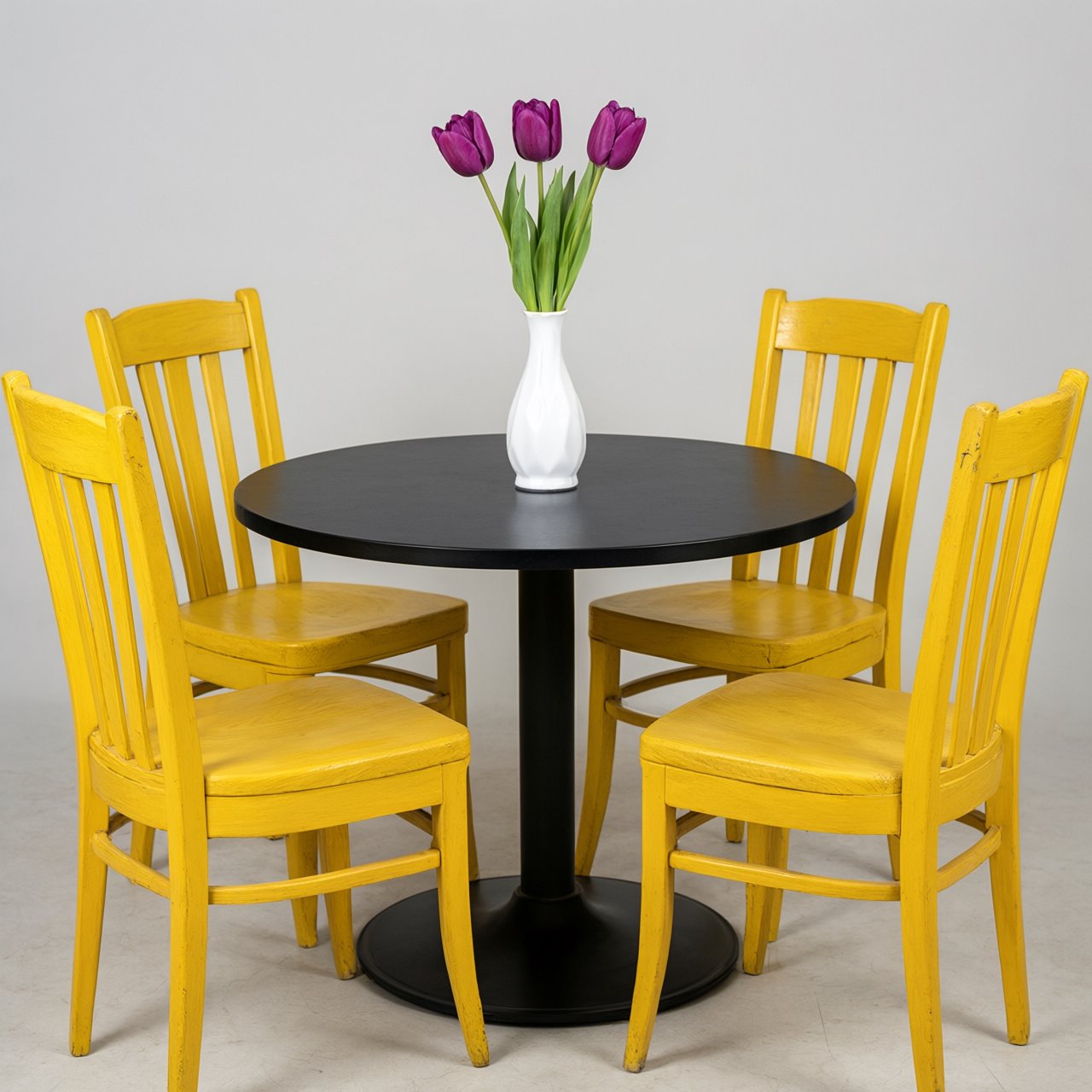 Exactly four yellow wooden chairs surround a round black table: two chairs at the front, one on the left, and one on the right. A white vase with three purple tulips sits at the table center, nothing else. — Qwen Image 3.0 Pro