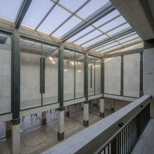 A soaring civic atrium in contemporary Italian Rationalist style pairs pale travertine, bronze mullions, and terrazzo beneath a glazed roof; cool morning light falls from above, viewed from a mezzanine, with aligned bays and credible supports. — Grok Imagine Image Quality