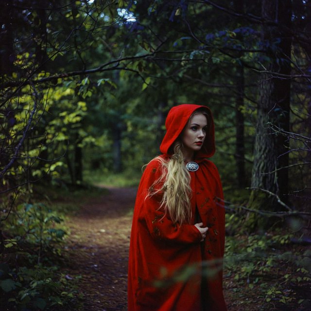 Medium shot at eye level: 1960s vintage film aesthetic. An adult woman with long, blonde hair walks alone through a dark forest. She wears a red hooded cloak, with the hood pulled up and fastened at the neck by a silver buckle. Photorealistic 1960s Technicolor film grain; soft, shallow depth of field. — Grok Imagine Image Quality