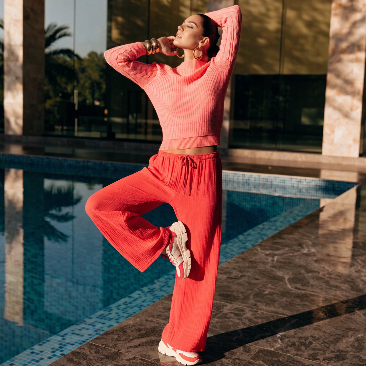Editorial glamour photograph of one adult woman in coral fitness wear stretching beside a sunlit indoor pool, natural posture, soft reflections, flattering golden light, refined athletic campaign mood. — Recraft v4 Pro