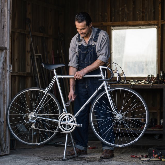 Candid documentary photograph of an adult repairing a bicycle at a quiet curbside workshop, cool morning window light, 50mm lens with shallow depth of field, grease smudges on their fingertips. — Kling v3 Omni