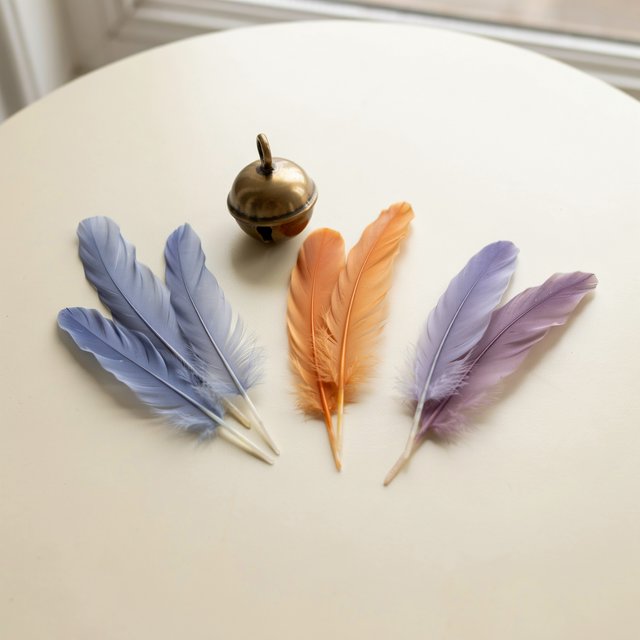 Exactly seven feathers lie on a cream tabletop: three blue on the left, two orange in the center, and two purple on the right. A brass bell sits above the orange pair, nothing else. — Ideogram v4