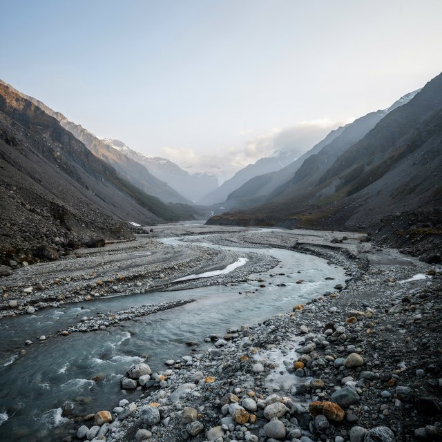 Beyond a braided glacier-fed stream, a steep moraine valley opens beneath clearing dawn snow flurries; gritty ice grains and water-polished stones sharpen the near bank, while layered ridges fade into cloud. — Model 8