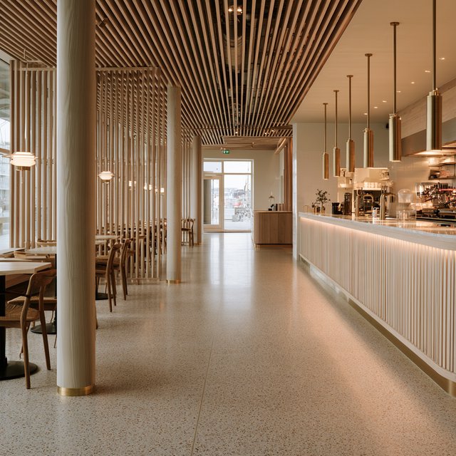 Inside an empty harbor café, restrained Danish modern design pairs ash slat screens, pale terrazzo, and brushed brass; overcast window light reaches the counter, viewed from the entrance, with aligned joinery and believable supports. — Model 13