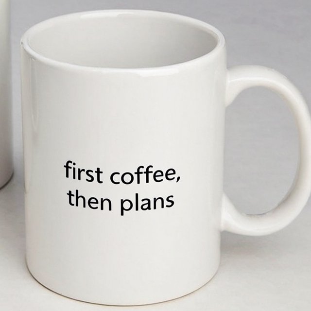 A white ceramic mug on a desk with the words "first coffee, then plans" printed in black lowercase sans-serif. — Krea 2 Large