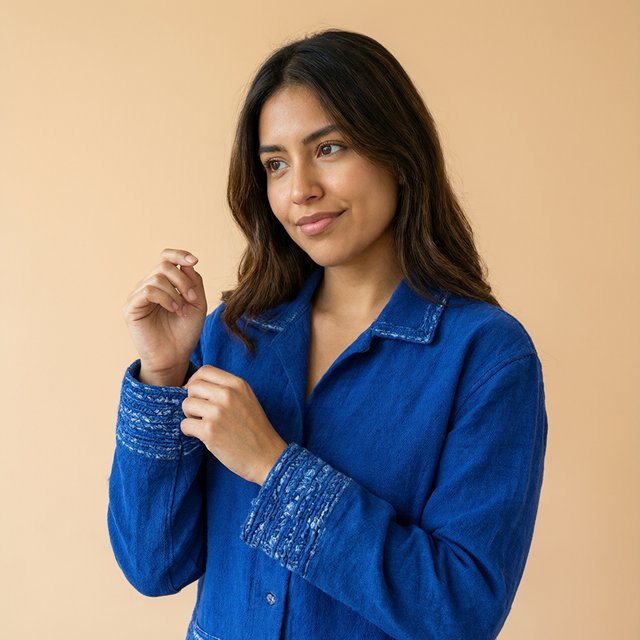 Fashion portrait of an adult Latina woman in her late 20s wearing a handwoven cobalt-blue cotton jacket, one hand touching its embroidered cuff, curious half-smile, against a pale peach studio backdrop, soft diffused window light shaping her face. — Qwen Image 3.0 Pro