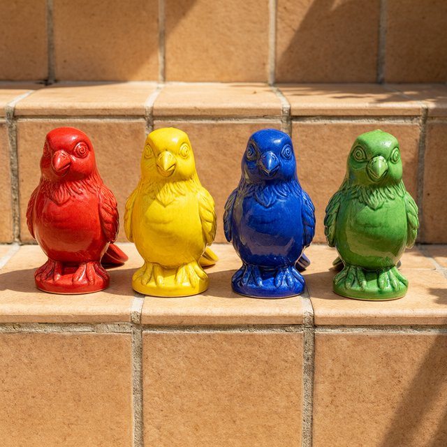 On a sunlit tiled ledge, exactly four ceramic bird figurines form a row: red at far left, yellow at left-center, blue at right-center, and green at far right; all face forward, nothing else. — Qwen Image 3.0 Pro