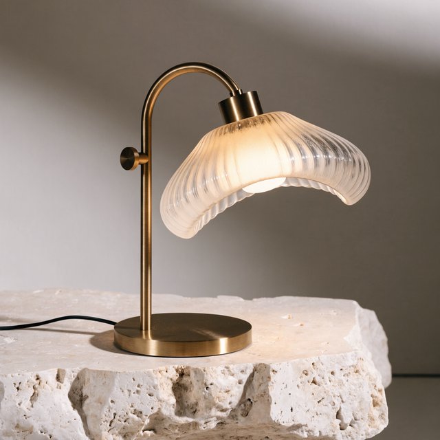 Commercial product photograph of an unbranded sculptural desk lamp made from brushed brass and opal glass, resting on pale travertine, against a warm gray background, with soft diffused light from upper left and gentle grounding shadow. — Recraft v4 Pro
