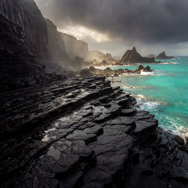 A rugged volcanic coastline under clearing storm clouds at late afternoon, black basalt shelves descending into turquoise surf, sea spray clinging to jagged rocks, tide pools reflecting distant cliffs and layered mountains fading into rain haze. — Krea 2 Large