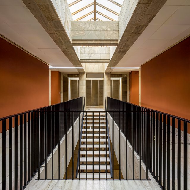 Beneath a pale limestone stairwell, a restrained mid-century modern interior frames a straight oak stair with blackened-steel stringers and limestone landings; afternoon clerestory light, viewed from the upper landing, reveals credible connections and aligned geometry. — Kling v3