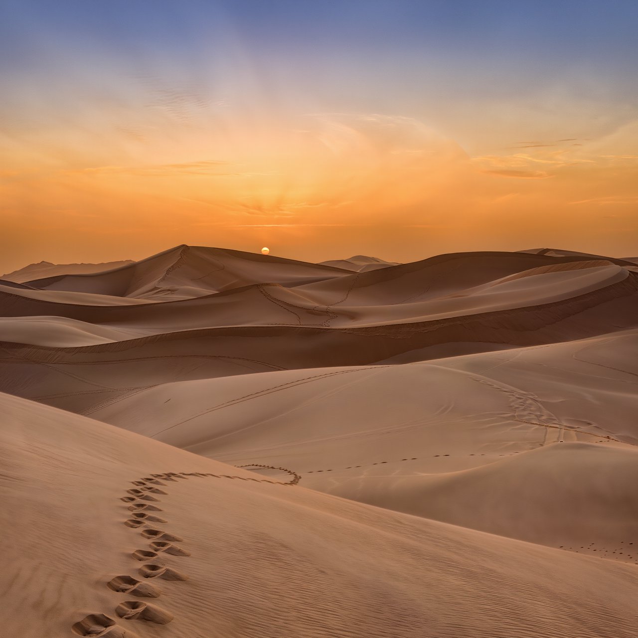 Sand dunes at sunset with wind-blown ridges, one set of footprints, deep blue sky fading to orange. — Kling v3