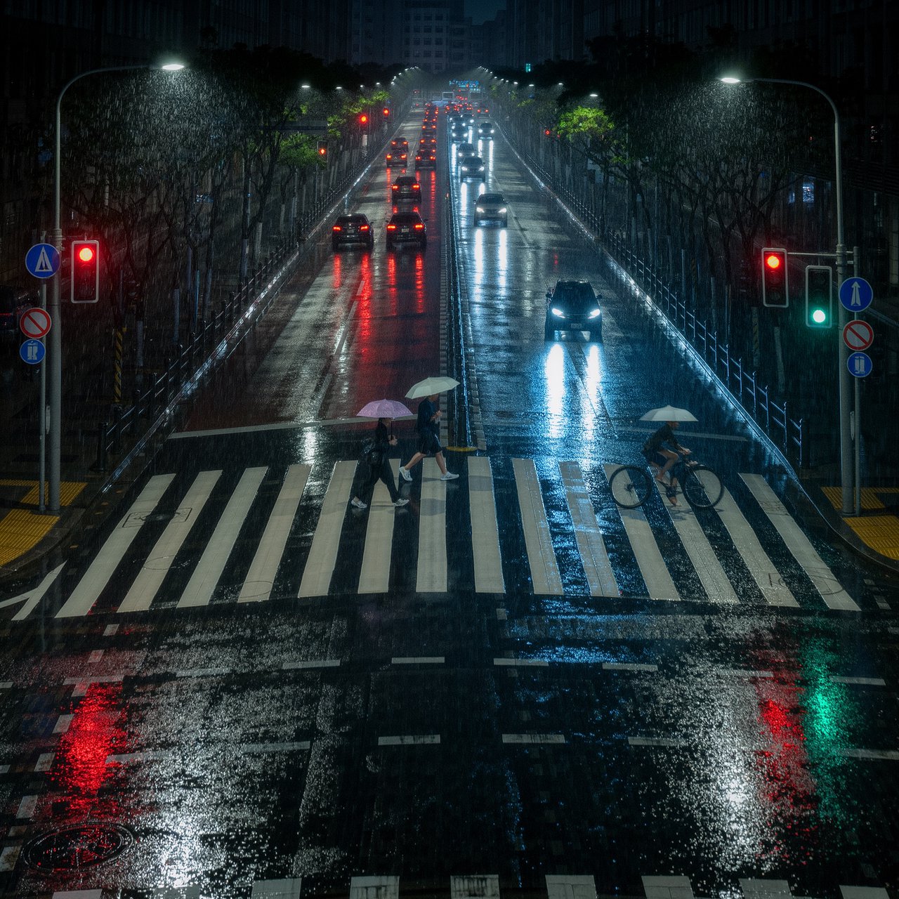 A rain-soaked city crosswalk at night seen from across the street, umbrellas, reflections of traffic lights on wet asphalt, slight motion blur on a passing cyclist. — Kling v3 Omni