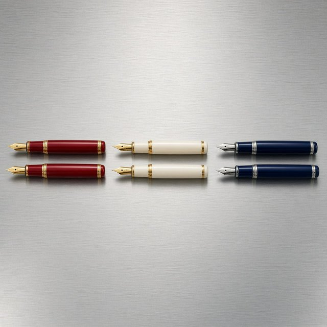 Across a brushed steel counter, exactly six fountain pens rest in three groups: two crimson pens on the left, two ivory pens in the center, and two cobalt pens on the right; nothing else. — Grok Imagine Image 2
