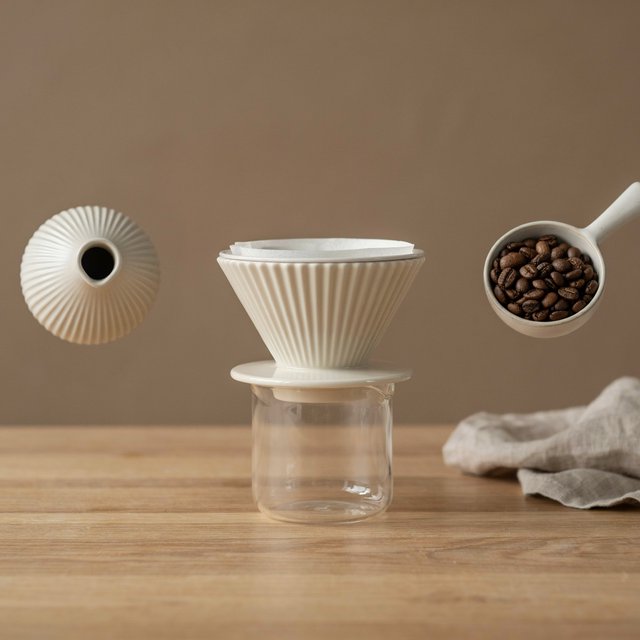 From directly overhead, an unbranded pour-over coffee set with ribbed porcelain and clear borosilicate components arranged in sequence on pale oak; warm taupe background, broad diffused softbox light and gentle side fill shape this commercial product image, no lettering. — Model 8