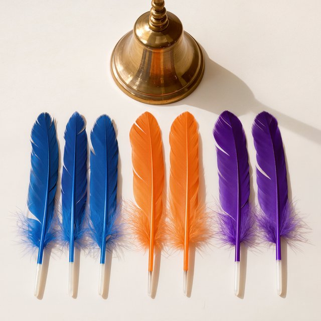 Exactly seven feathers lie on a cream tabletop: three blue on the left, two orange in the center, and two purple on the right. A brass bell sits above the orange pair, nothing else. — Kling v3