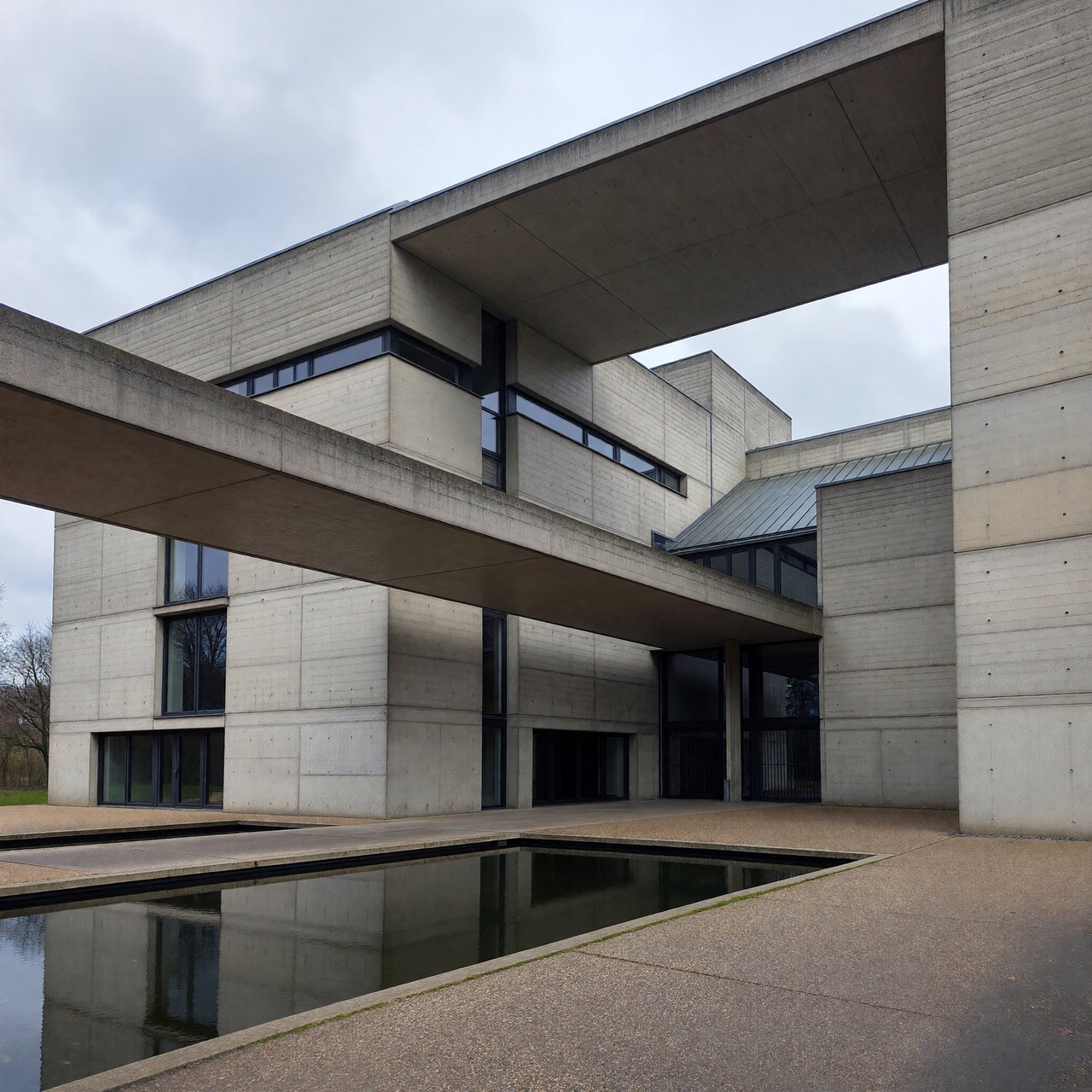 Exterior of a compact brutalist art museum, pale board-formed concrete, deep rectangular window recesses, a broad cantilevered entrance canopy, low reflecting pool, overcast afternoon light, viewed from a quiet plaza at eye level, crisp orthogonal architectural photography. — ImagineArt 1.5 Pro