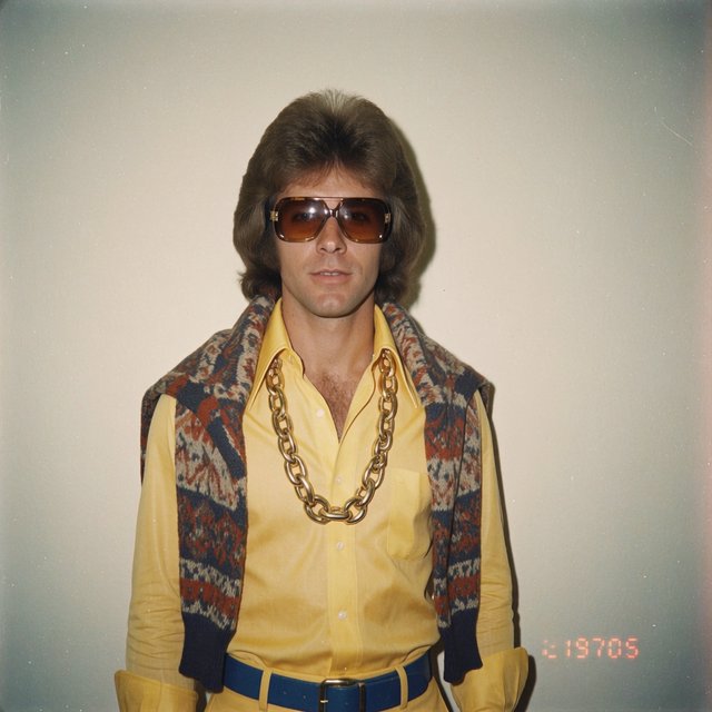 Create an image of a man in the quintessential style of 1975. Style his hair, clothing, accessories, and surroundings to reflect the distinctive look of the mid-1970s—featuring bold silhouettes, eye-catching accessories, layered details, and characteristic colors and textures. Give the image the feel of an authentic 1975 photograph, complete with analog film grain, faded colors, direct flash lighting, and a slight soft-focus effect. Add a period-accurate, red-orange date stamp in a 1970s style in one of the bottom corners. No recognizable posters. No modern objects or text. — Krea 2 Medium